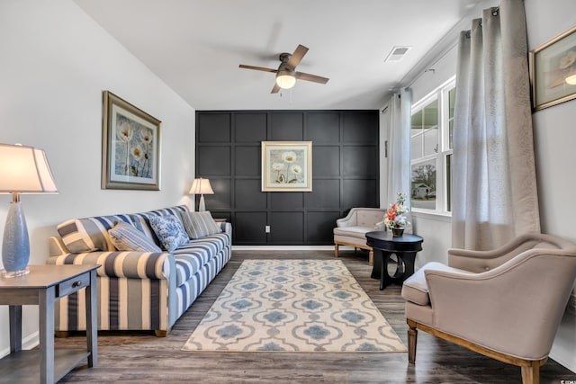 living room with a ceiling fan, visible vents, a decorative wall, and wood finished floors