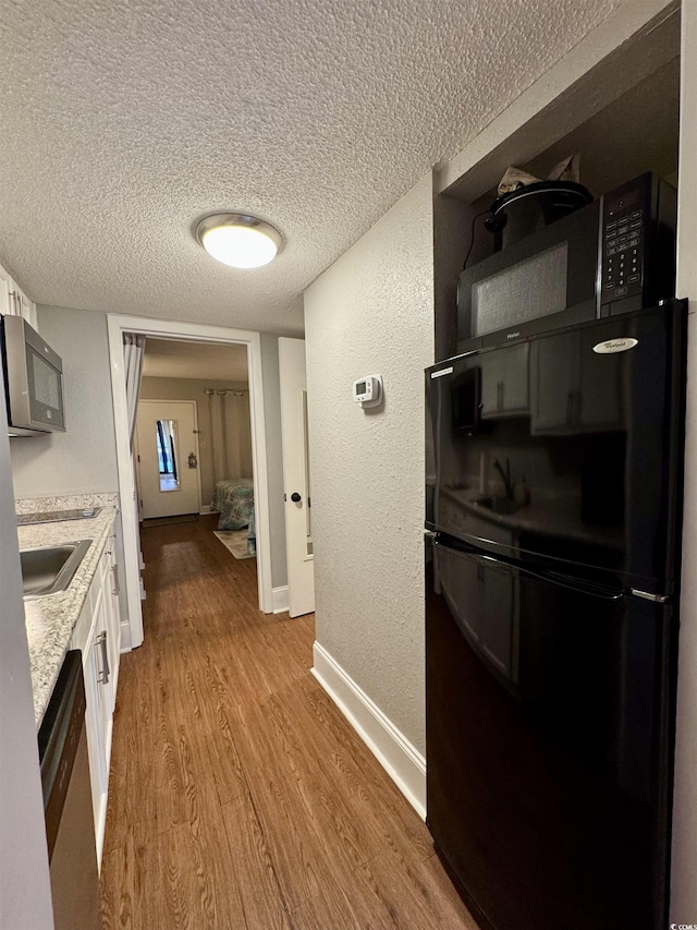 kitchen with black fridge, white cabinetry, light hardwood / wood-style flooring, a textured ceiling, and stainless steel dishwasher