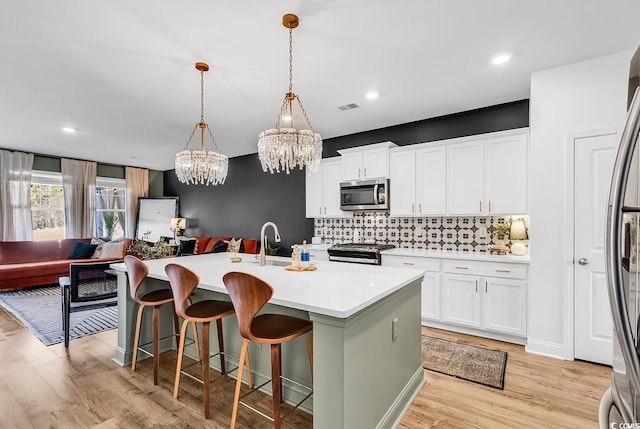 kitchen featuring pendant lighting, a kitchen island with sink, white cabinetry, stainless steel appliances, and light hardwood / wood-style floors