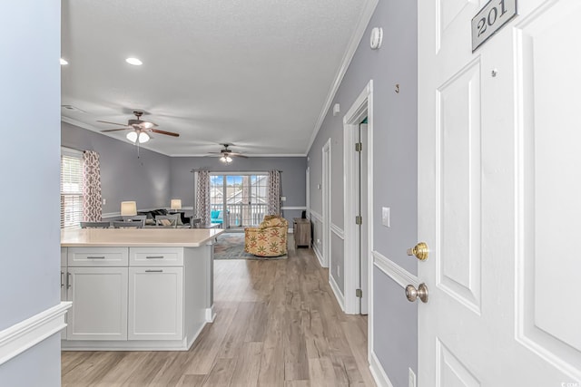 kitchen featuring a textured ceiling, light hardwood / wood-style flooring, ornamental molding, and white cabinets