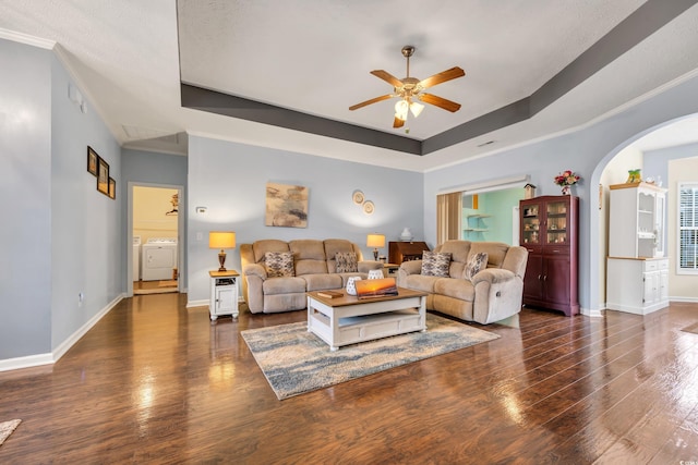 living room featuring dark wood-style floors, a raised ceiling, washer / dryer, and baseboards