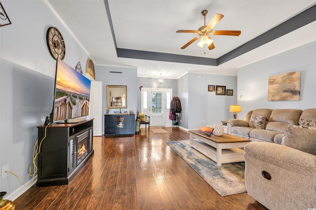 living room featuring baseboards, dark wood-style floors, ceiling fan, a tray ceiling, and crown molding