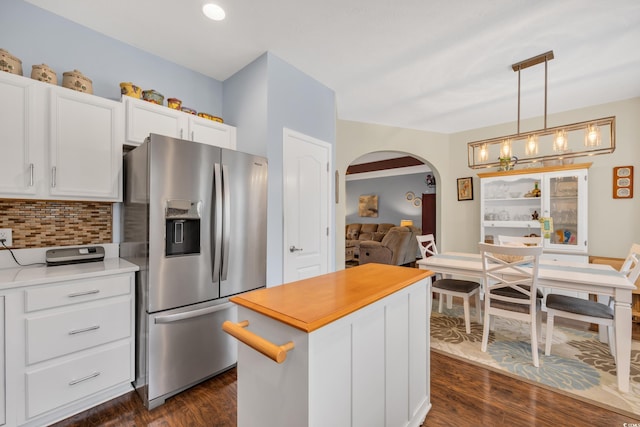 kitchen with arched walkways, a kitchen island, white cabinetry, hanging light fixtures, and stainless steel fridge