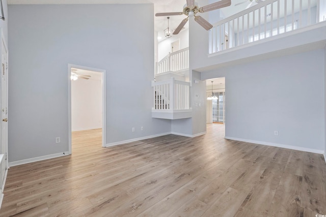 unfurnished living room featuring baseboards, light wood finished floors, and ceiling fan with notable chandelier