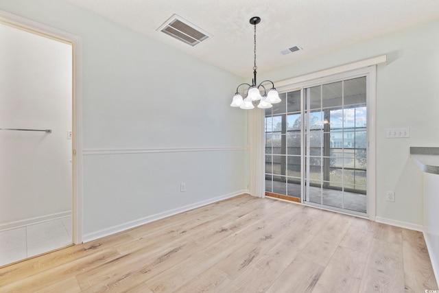 unfurnished dining area featuring visible vents, a chandelier, and wood finished floors