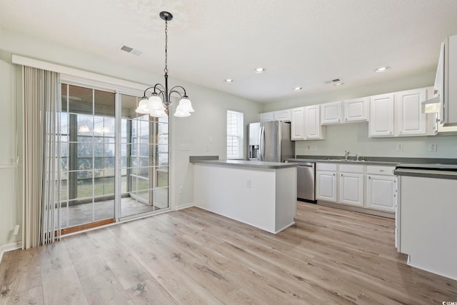 kitchen featuring stainless steel appliances, dark countertops, hanging light fixtures, white cabinetry, and a peninsula