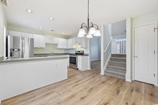 kitchen featuring appliances with stainless steel finishes, under cabinet range hood, white cabinetry, pendant lighting, and a sink