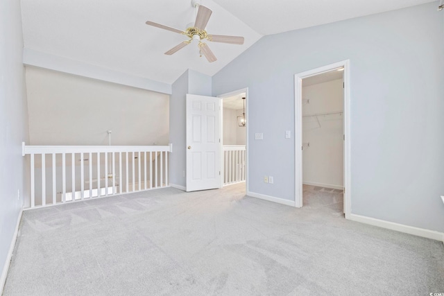 empty room featuring a ceiling fan, light carpet, vaulted ceiling, and baseboards