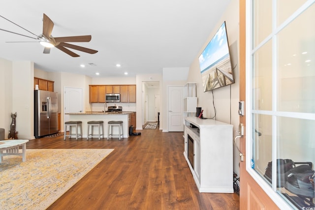 kitchen featuring dark wood-style floors, appliances with stainless steel finishes, brown cabinets, a kitchen island with sink, and a kitchen bar