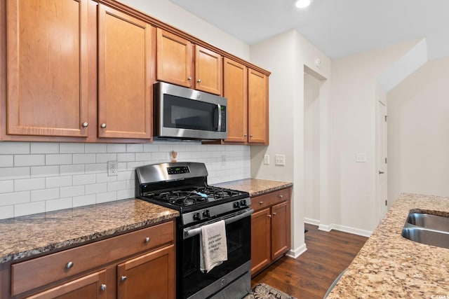 kitchen featuring light stone counters, brown cabinets, dark wood finished floors, decorative backsplash, and appliances with stainless steel finishes