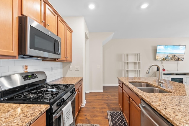 kitchen featuring dark wood finished floors, tasteful backsplash, appliances with stainless steel finishes, a sink, and light stone countertops