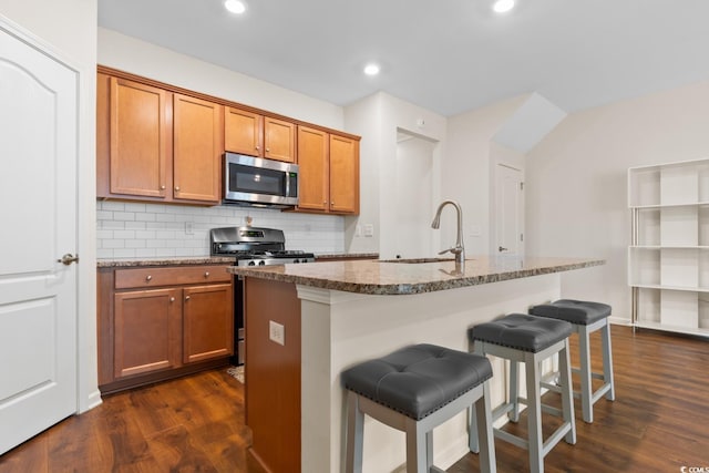 kitchen featuring tasteful backsplash, brown cabinetry, dark wood-style flooring, stainless steel appliances, and a sink