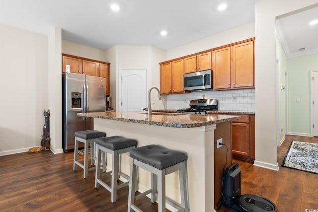 kitchen featuring a breakfast bar area, backsplash, appliances with stainless steel finishes, a sink, and dark stone counters