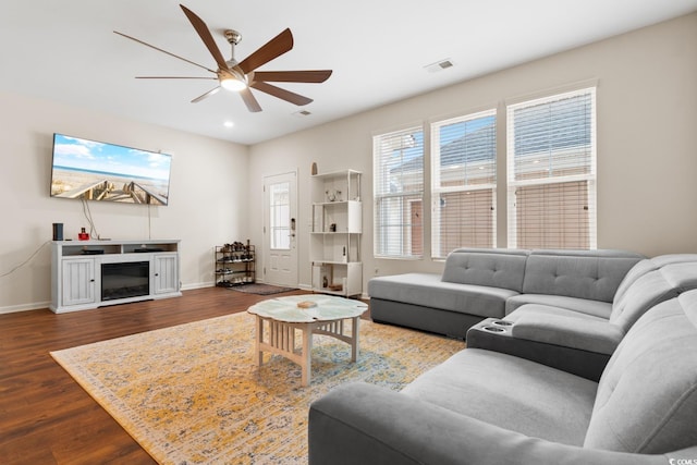 living area featuring visible vents, a ceiling fan, a glass covered fireplace, wood finished floors, and baseboards