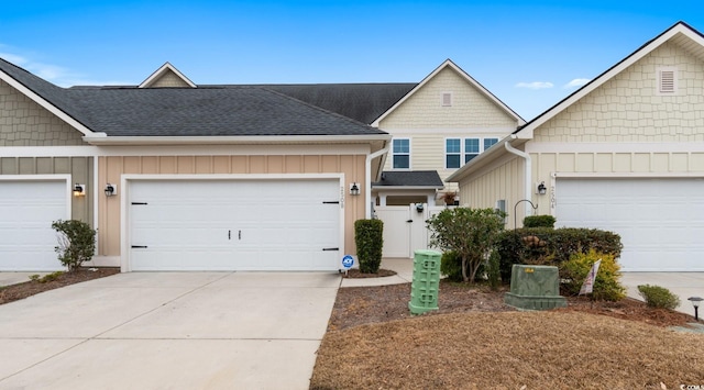 view of property featuring an attached garage, a shingled roof, driveway, a gate, and board and batten siding