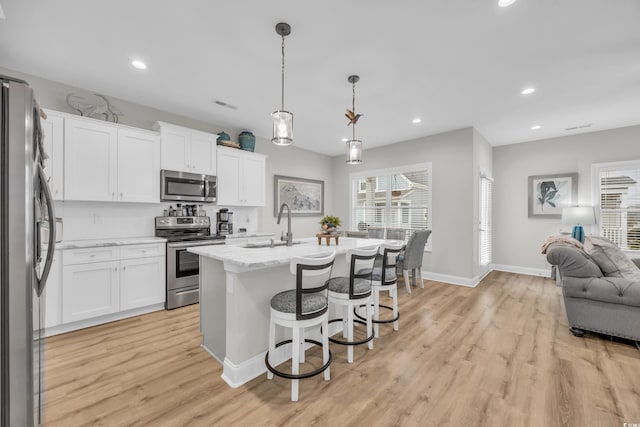 kitchen featuring stainless steel appliances, an island with sink, hanging light fixtures, and white cabinets