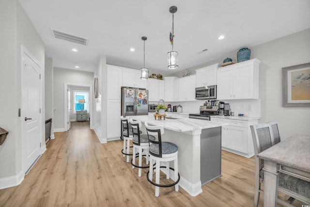 kitchen featuring a kitchen island, appliances with stainless steel finishes, white cabinetry, a kitchen breakfast bar, and hanging light fixtures