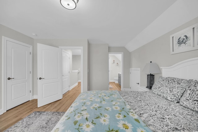 bedroom with wood-type flooring, ensuite bathroom, and vaulted ceiling