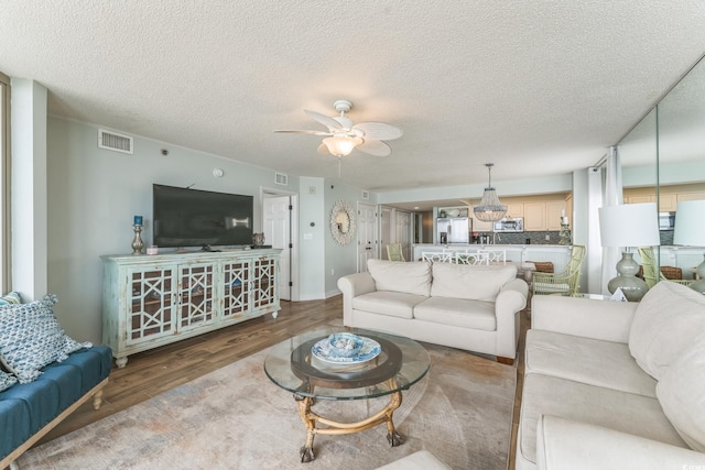 living area featuring a textured ceiling, a ceiling fan, visible vents, and light wood-type flooring