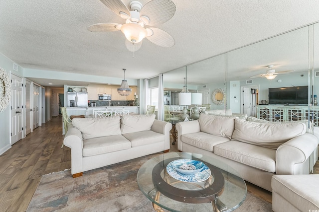 living area featuring visible vents, a textured ceiling, a ceiling fan, and dark wood-style flooring