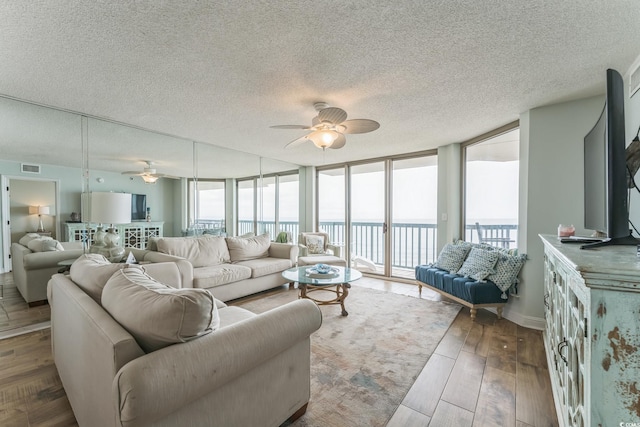 living room with visible vents, expansive windows, a textured ceiling, wood finished floors, and ceiling fan