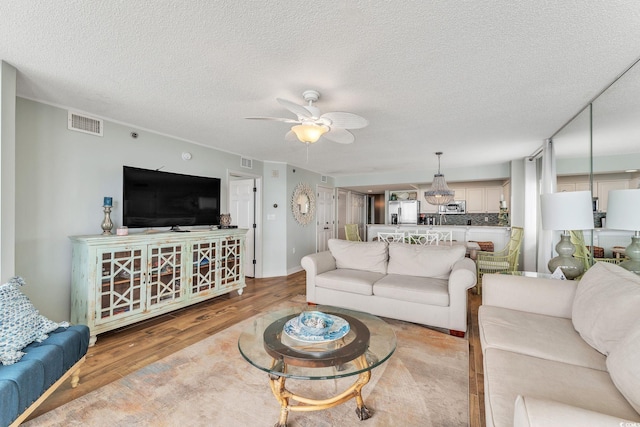 living room featuring visible vents, a textured ceiling, light wood-style floors, and a ceiling fan