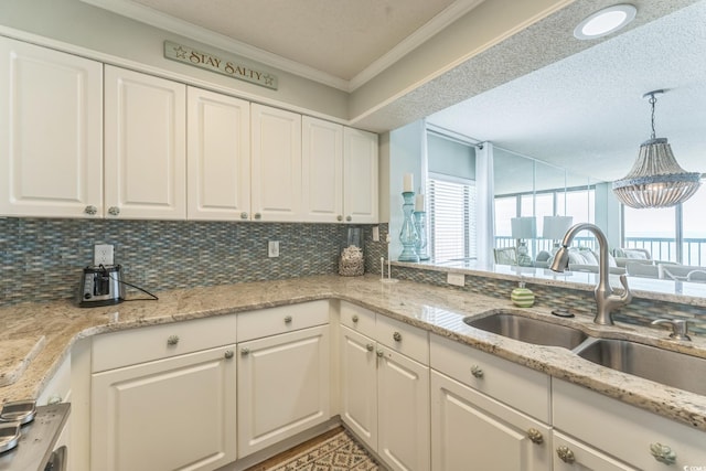 kitchen with a sink, tasteful backsplash, ornamental molding, and white cabinetry