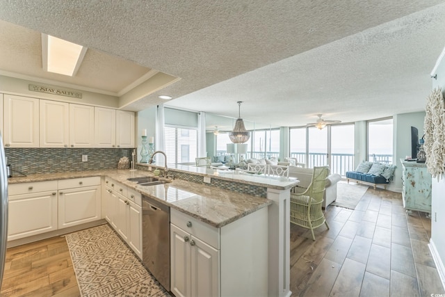 kitchen featuring a peninsula, a sink, open floor plan, dishwasher, and tasteful backsplash