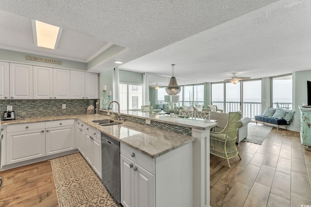 kitchen with open floor plan, a peninsula, stainless steel dishwasher, and a sink