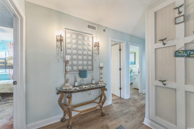 corridor with visible vents, wood finished floors, baseboards, and a textured ceiling