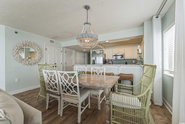 dining area featuring wood finished floors, visible vents, baseboards, a textured ceiling, and a notable chandelier