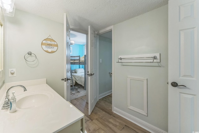 ensuite bathroom featuring a textured ceiling, ensuite bath, wood finished floors, and vanity