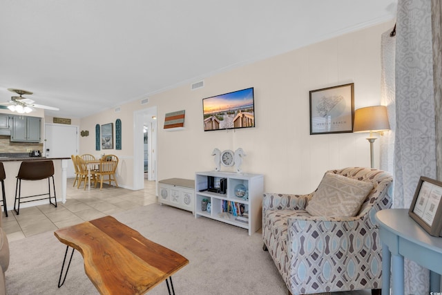 living area with light carpet, light tile patterned flooring, ceiling fan, and crown molding
