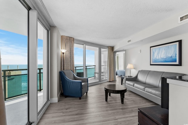 living room featuring a water view, light hardwood / wood-style floors, a textured ceiling, and expansive windows