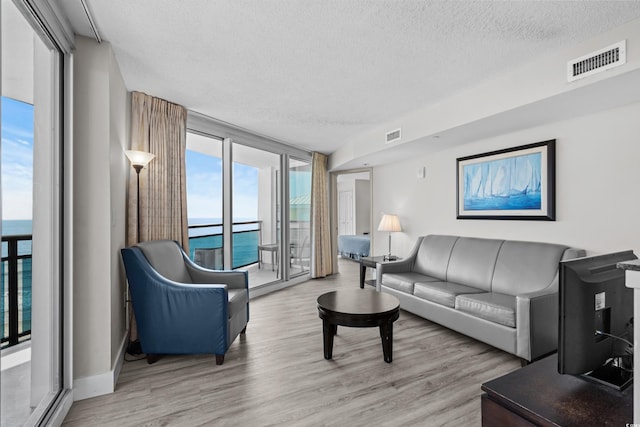 living room featuring a textured ceiling, a wall of windows, a water view, and light hardwood / wood-style floors