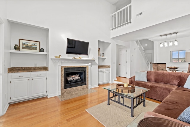 living room with built in shelves, a tiled fireplace, a high ceiling, and light wood-type flooring