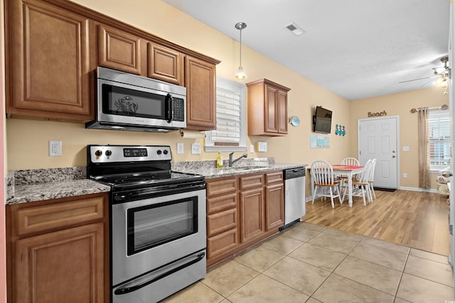 kitchen with appliances with stainless steel finishes, sink, light tile patterned floors, ceiling fan, and light stone counters