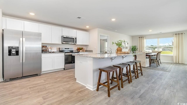 kitchen with sink, appliances with stainless steel finishes, an island with sink, light hardwood / wood-style floors, and white cabinets