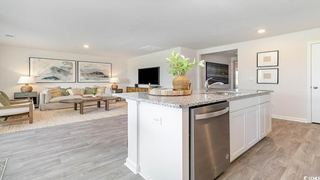 kitchen with an island with sink, dishwasher, sink, white cabinets, and light stone counters