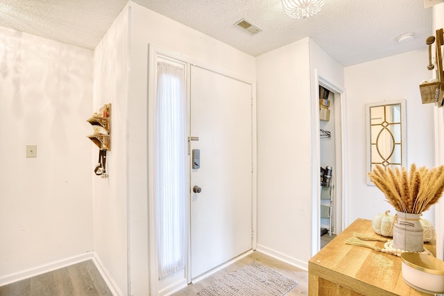 entrance foyer featuring light wood-style floors, baseboards, visible vents, and a textured ceiling