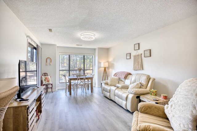 living room with baseboards, a textured ceiling, visible vents, and wood finished floors