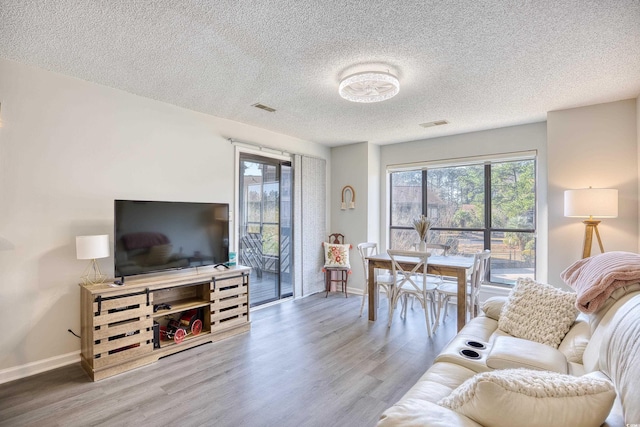 living room featuring visible vents, a textured ceiling, baseboards, and wood finished floors
