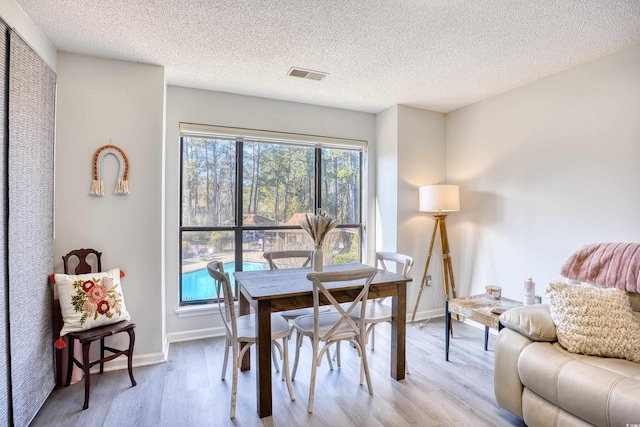 dining space featuring light wood-style flooring, a textured ceiling, visible vents, and baseboards