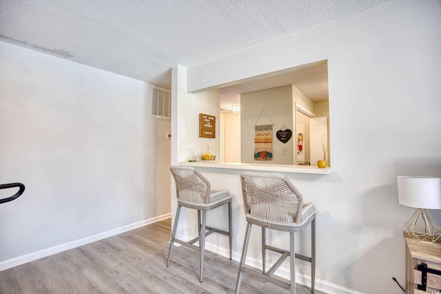 kitchen featuring a textured ceiling, a breakfast bar area, wood finished floors, and baseboards