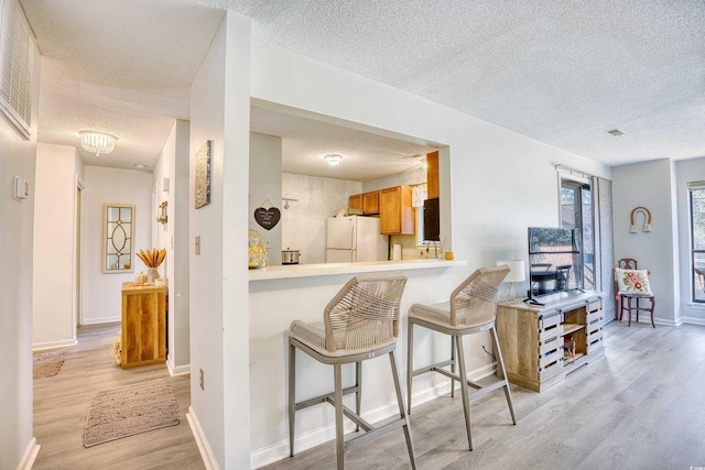 kitchen featuring light countertops, light wood-style floors, freestanding refrigerator, a textured ceiling, and a kitchen bar
