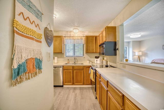 kitchen with brown cabinets, light countertops, light wood-style flooring, appliances with stainless steel finishes, and a sink