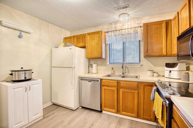 kitchen with appliances with stainless steel finishes, light wood-type flooring, light countertops, and a sink