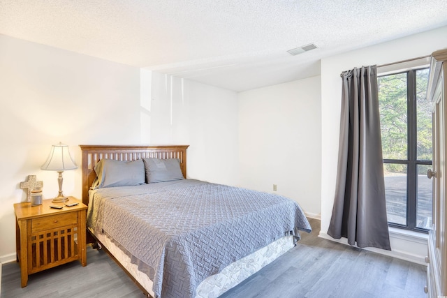 bedroom with visible vents, a textured ceiling, baseboards, and wood finished floors