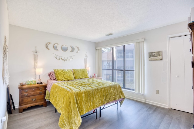 bedroom featuring light wood-type flooring, baseboards, visible vents, and a textured ceiling