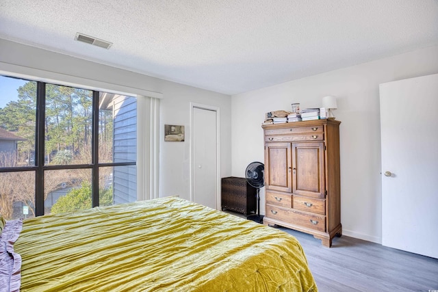 bedroom featuring light wood-type flooring, visible vents, a textured ceiling, and baseboards